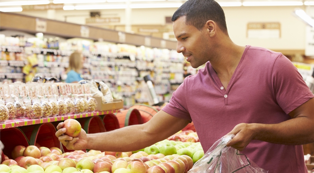 Man selecting a piece of fruit at the grocery store to help form healthier eating habits on the road