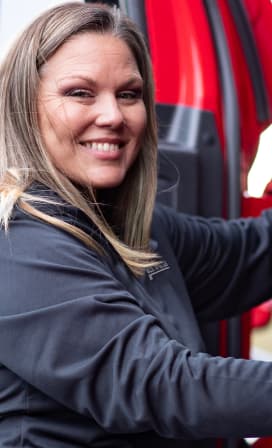 White female U.S. Xpress driver smiling climbing into truck.