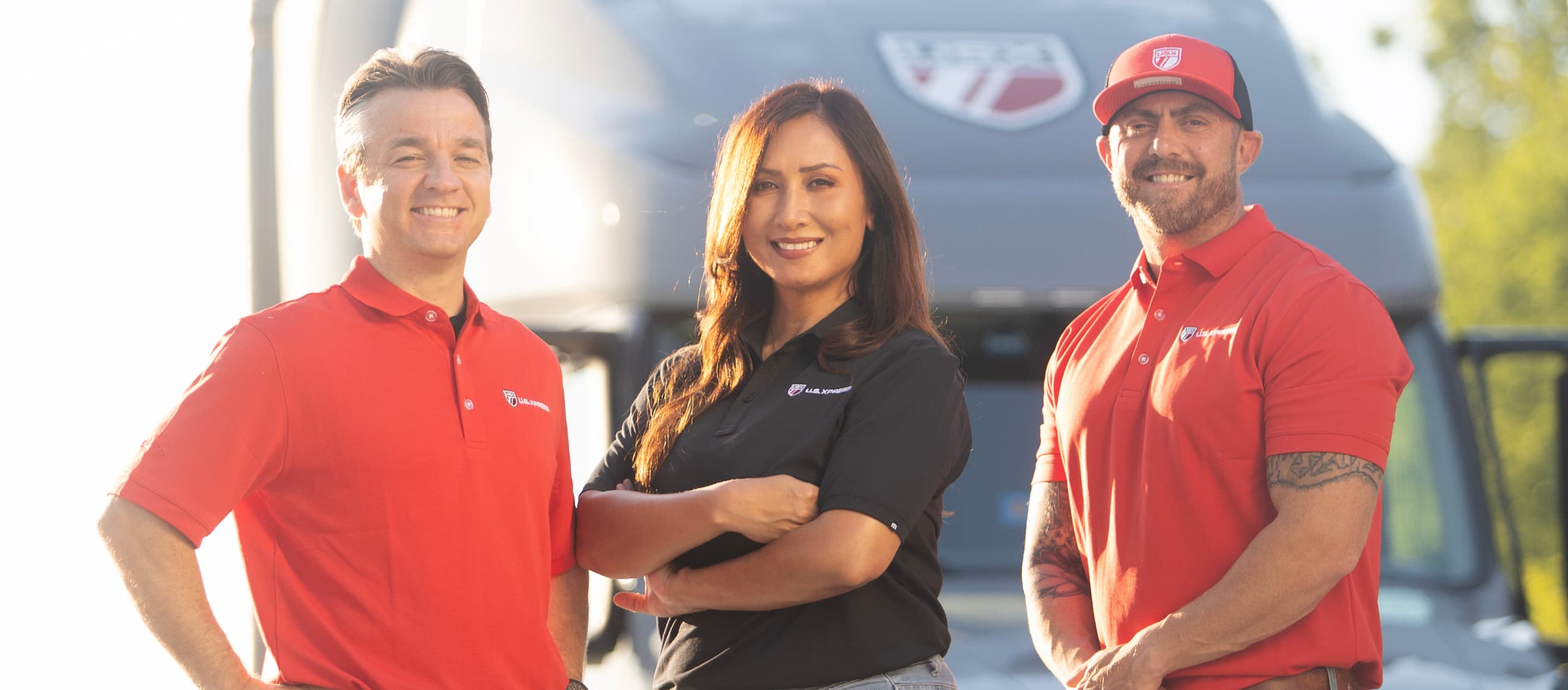 Three U.S. Xpress team members smiling in front of a U.S. Xpress truck.